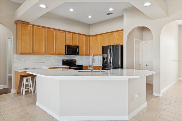 kitchen featuring arched walkways, light tile patterned floors, visible vents, black appliances, and a center island with sink