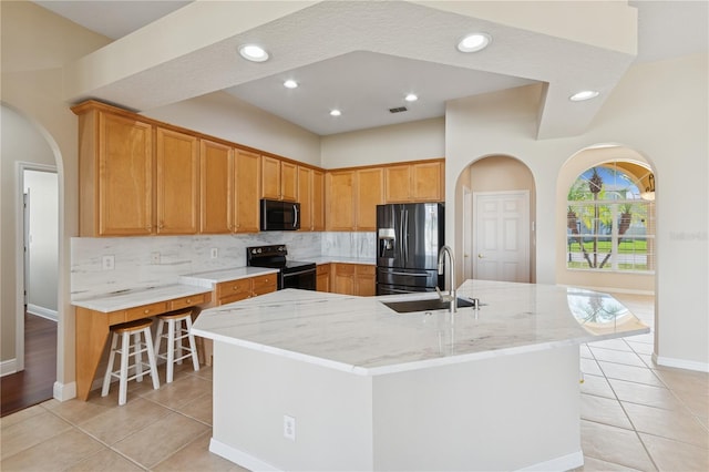 kitchen featuring arched walkways, decorative backsplash, black appliances, a sink, and light tile patterned flooring