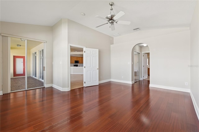 empty room with arched walkways, visible vents, ceiling fan, wood finished floors, and baseboards