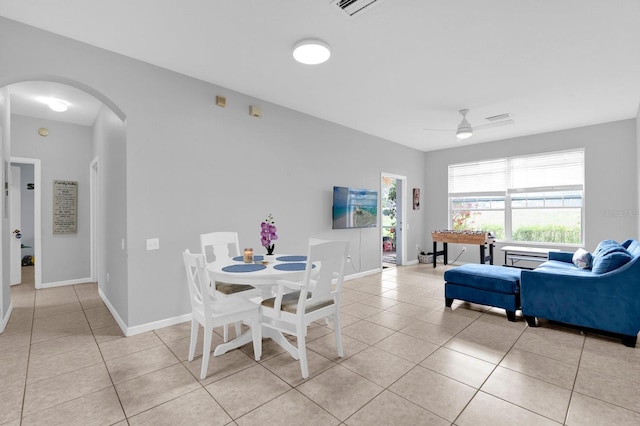 dining area featuring light tile patterned floors, ceiling fan, arched walkways, and baseboards