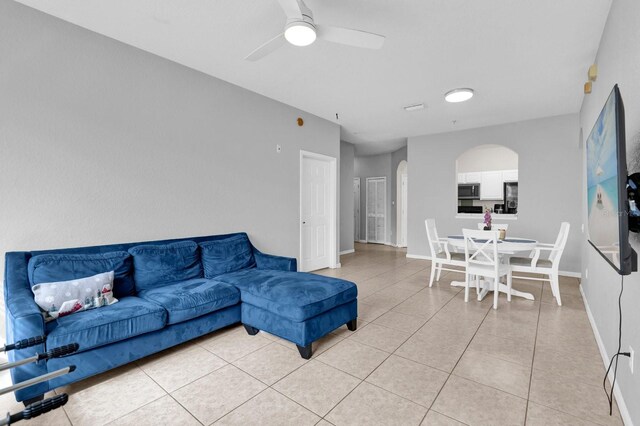 living room featuring arched walkways, light tile patterned flooring, ceiling fan, and baseboards