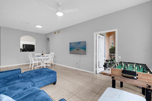 living area with arched walkways, ceiling fan, tile patterned flooring, and baseboards