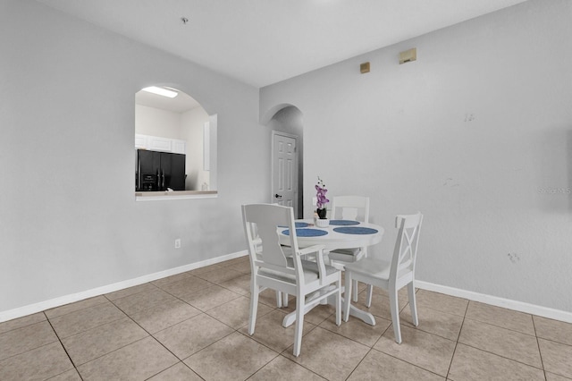 dining room featuring arched walkways, tile patterned flooring, and baseboards