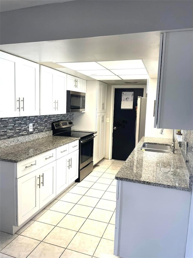 kitchen with light tile patterned floors, stainless steel appliances, backsplash, a sink, and dark stone countertops