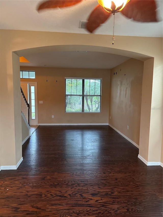 unfurnished living room with dark wood-style floors, baseboards, visible vents, and stairway