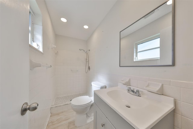 bathroom featuring a wainscoted wall, tile walls, toilet, a stall shower, and vanity