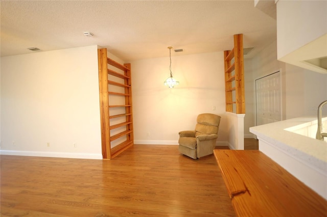 living area featuring a textured ceiling, wood finished floors, visible vents, and baseboards