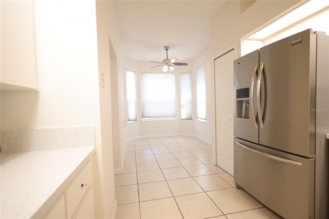 kitchen with light tile patterned floors, white cabinets, a ceiling fan, stainless steel fridge with ice dispenser, and light countertops