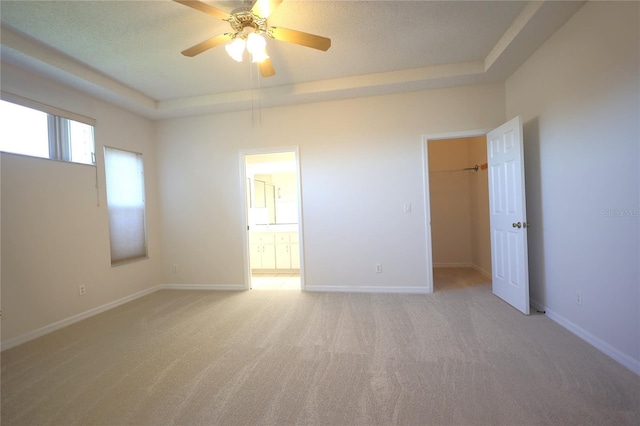 empty room with light carpet, ceiling fan, a tray ceiling, and baseboards