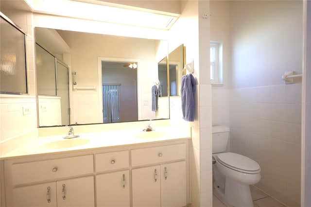 bathroom featuring double vanity, toilet, a shower with door, a sink, and tile walls