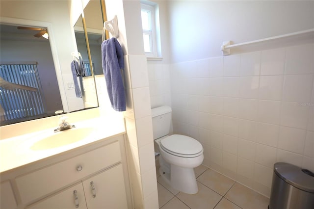 half bath with toilet, vanity, tile patterned flooring, and tile walls