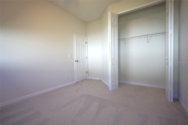 unfurnished bedroom featuring baseboards, a closet, lofted ceiling, and light colored carpet