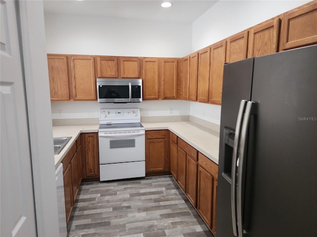 kitchen with light countertops, appliances with stainless steel finishes, a sink, and brown cabinets