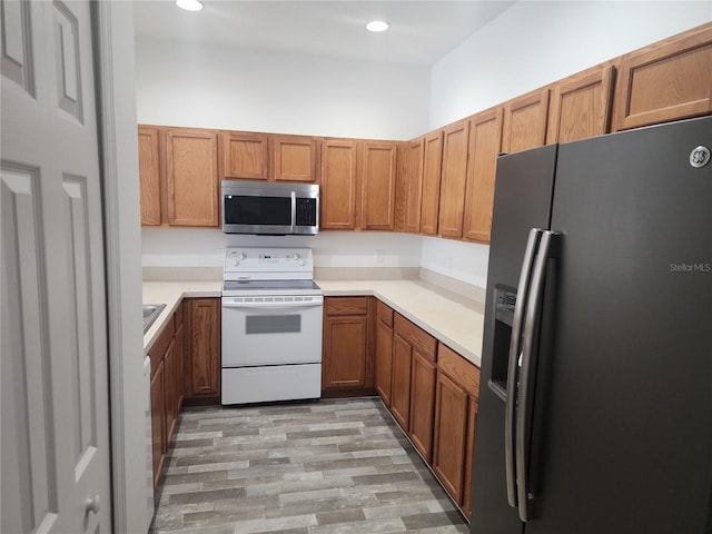 kitchen with recessed lighting, light countertops, appliances with stainless steel finishes, light wood-type flooring, and brown cabinetry