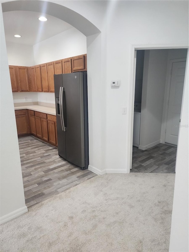 kitchen featuring light colored carpet, baseboards, light countertops, brown cabinetry, and stainless steel fridge