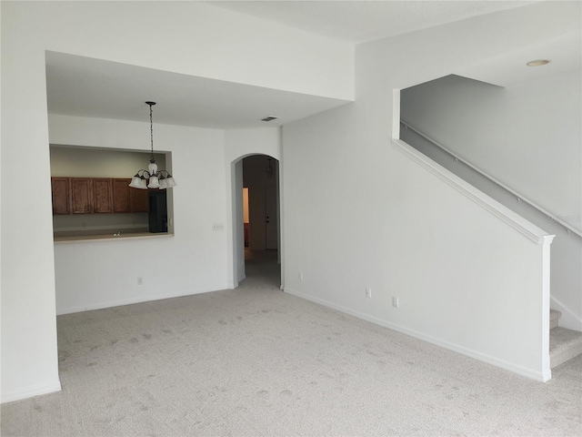 unfurnished living room with arched walkways, light colored carpet, visible vents, baseboards, and stairs