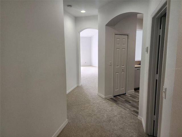 hallway with arched walkways, carpet flooring, and baseboards