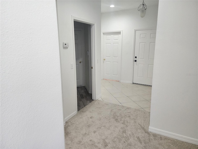 hallway featuring light tile patterned floors, baseboards, and light colored carpet