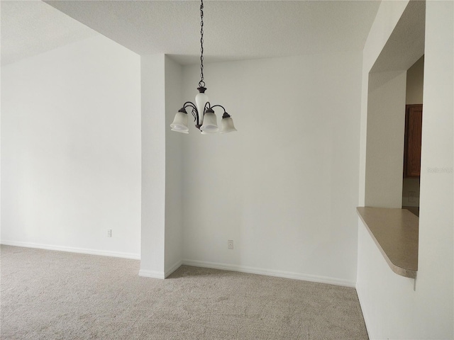 unfurnished dining area with carpet floors, an inviting chandelier, baseboards, and a textured ceiling