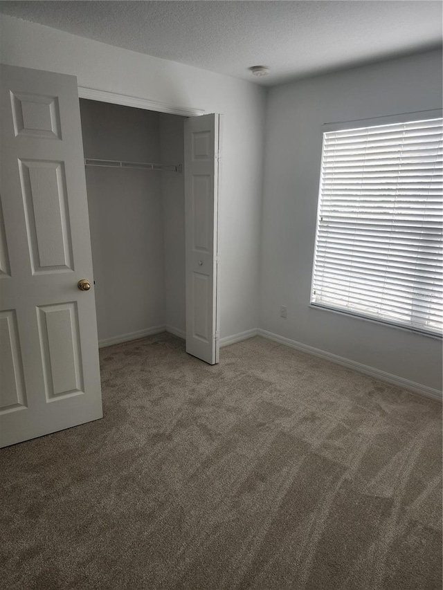 unfurnished bedroom with a textured ceiling, a closet, carpet, and baseboards