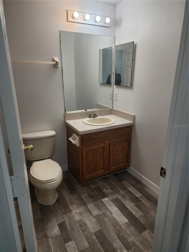 half bathroom featuring toilet, baseboards, wood finished floors, and vanity