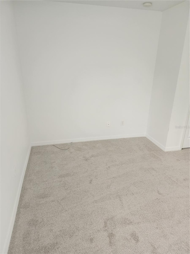 spare room featuring light carpet and baseboards