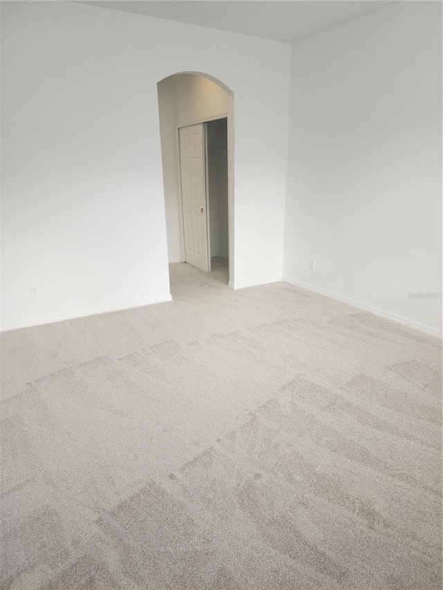 unfurnished room featuring arched walkways, baseboards, and light colored carpet