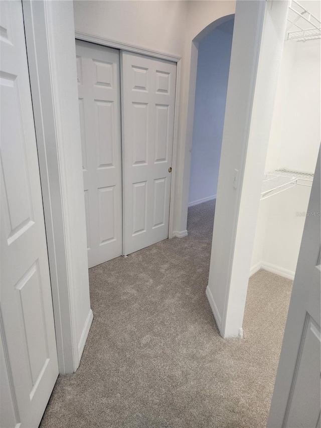 hallway featuring baseboards, arched walkways, and light colored carpet