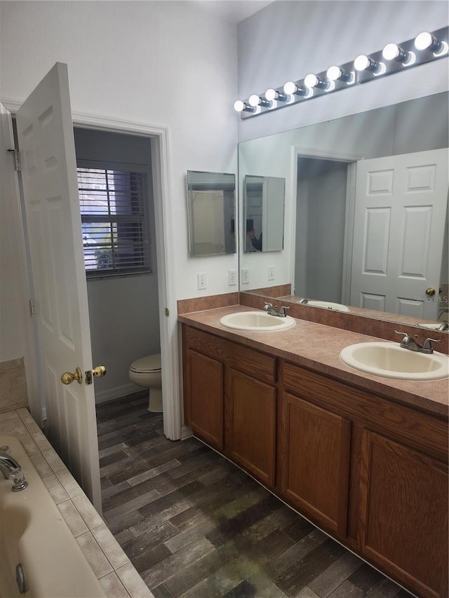 bathroom featuring double vanity, a sink, toilet, and wood finished floors