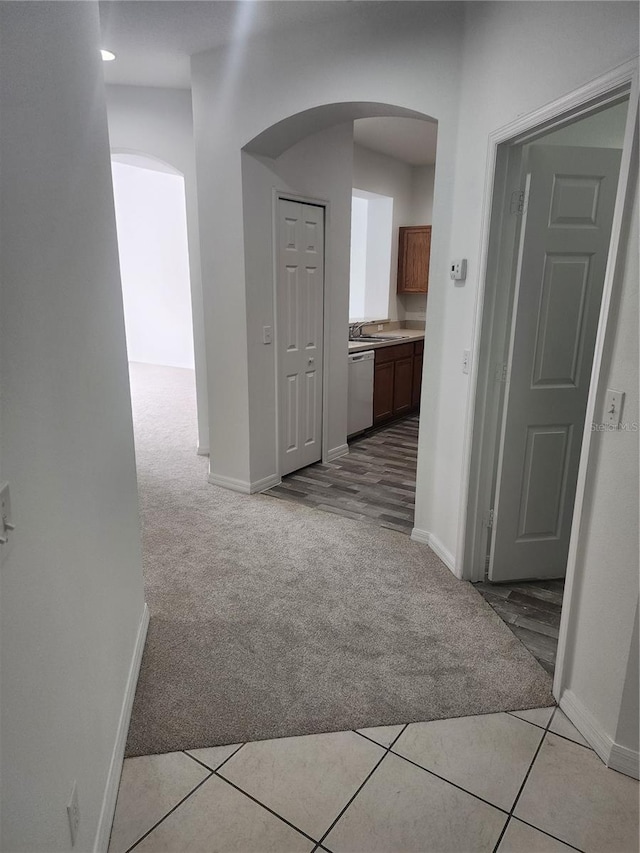 hallway with arched walkways, light carpet, and baseboards