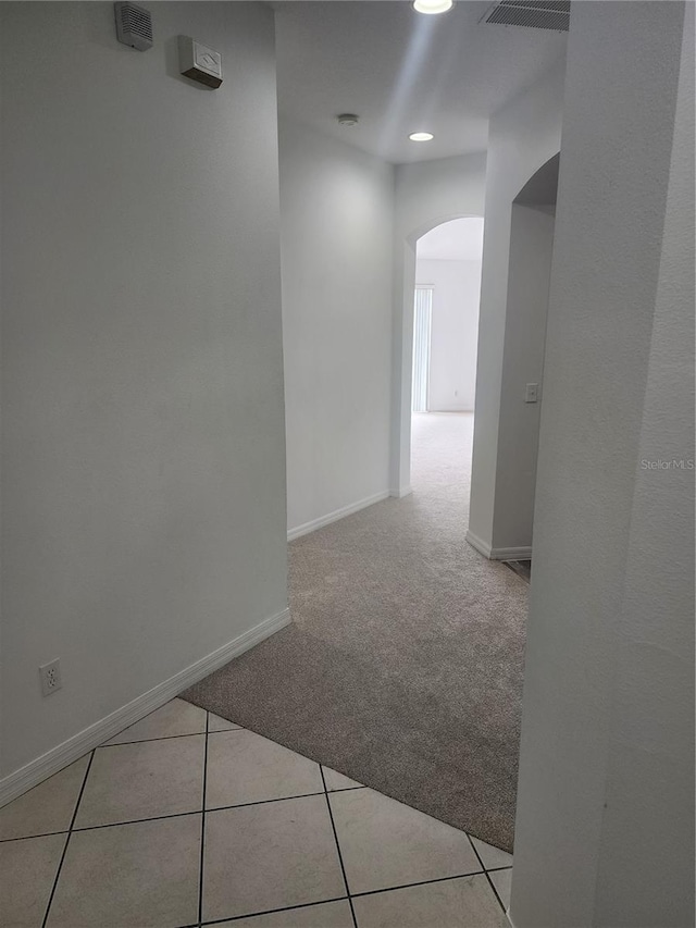 corridor with arched walkways, light colored carpet, baseboards, and light tile patterned floors