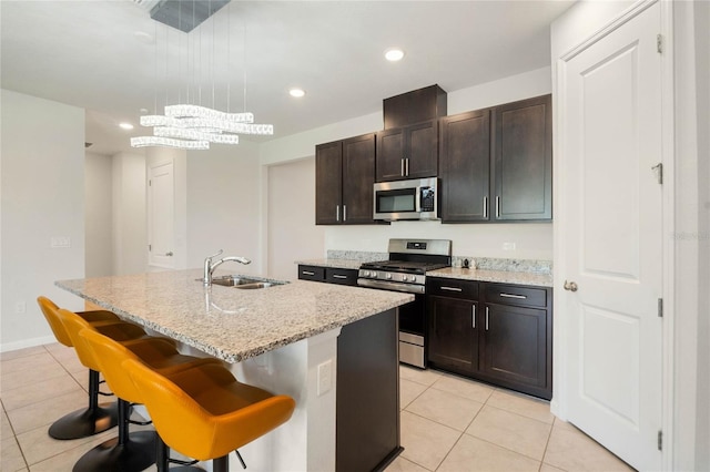 kitchen with stainless steel appliances, a sink, an island with sink, a kitchen bar, and pendant lighting