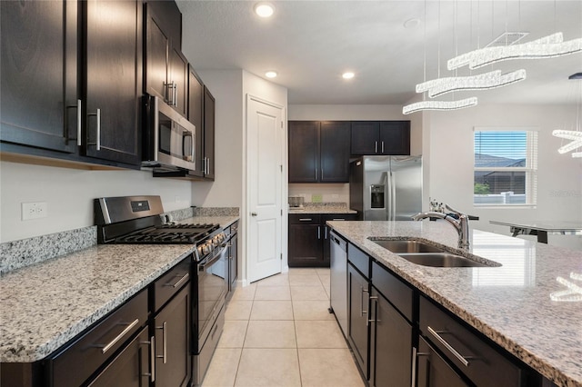 kitchen featuring light tile patterned floors, stainless steel appliances, a sink, hanging light fixtures, and an island with sink