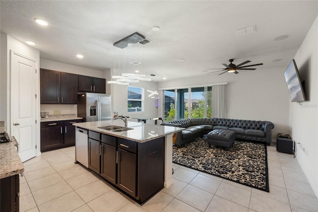 kitchen featuring light stone counters, a kitchen island with sink, open floor plan, hanging light fixtures, and appliances with stainless steel finishes