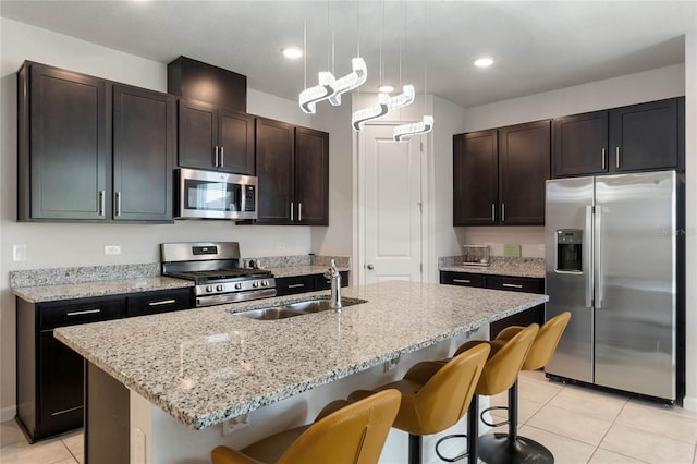 kitchen with stainless steel appliances, a kitchen island with sink, dark brown cabinetry, and decorative light fixtures