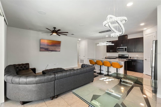 living area with light tile patterned floors, recessed lighting, ceiling fan with notable chandelier, visible vents, and baseboards