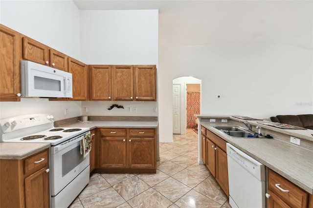 kitchen featuring white appliances, arched walkways, a towering ceiling, light countertops, and a sink