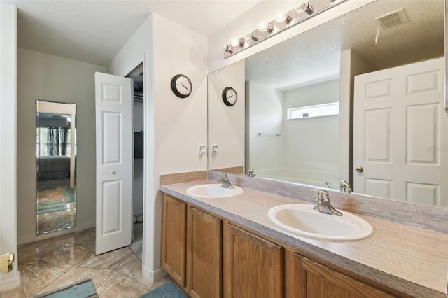 ensuite bathroom featuring visible vents, a sink, a textured ceiling, and double vanity