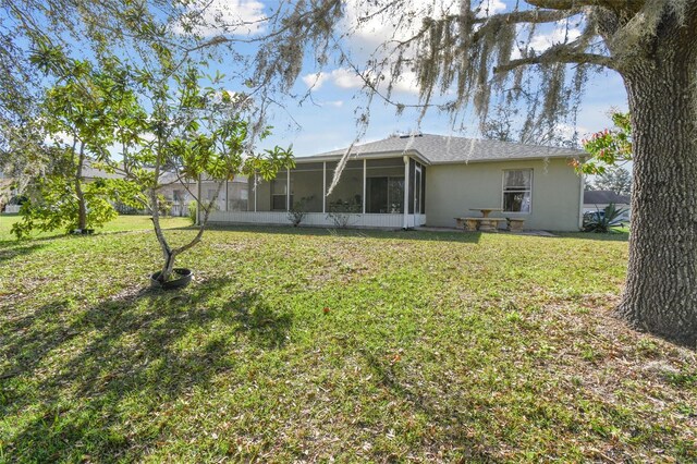 rear view of house with a sunroom, a lawn, and stucco siding