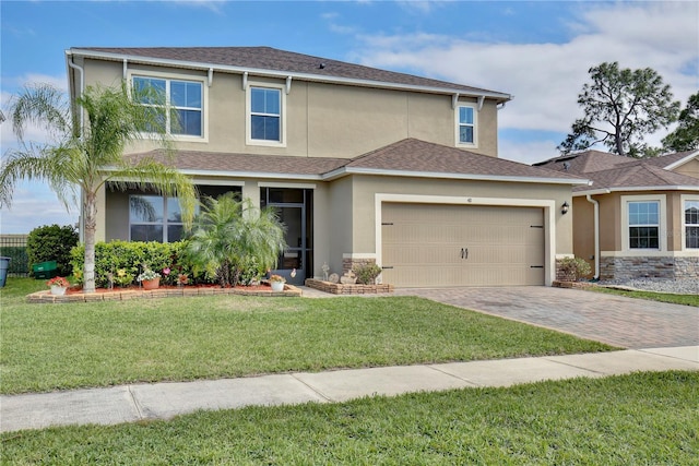 traditional-style home with an attached garage, a shingled roof, decorative driveway, stucco siding, and a front yard