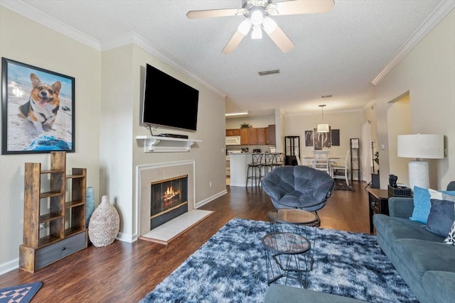 living room featuring ornamental molding, dark wood-type flooring, a textured ceiling, and a tile fireplace