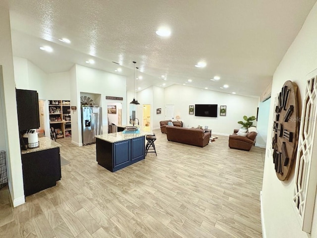 kitchen featuring a center island with sink, stainless steel fridge with ice dispenser, hanging light fixtures, open floor plan, and a kitchen breakfast bar