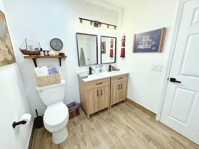 bathroom with a sink, double vanity, wood finished floors, and toilet