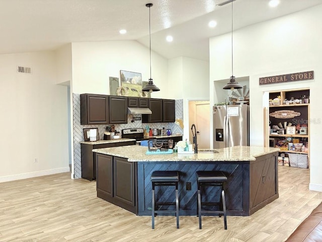 kitchen featuring pendant lighting, stainless steel appliances, a kitchen island with sink, dark brown cabinetry, and under cabinet range hood