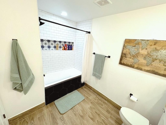 bathroom with baseboards, visible vents, toilet, wood finished floors, and tiled shower / bath combo