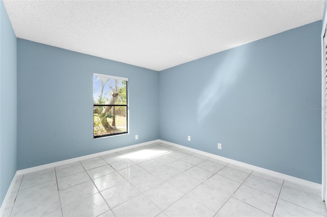 empty room featuring light tile patterned flooring, a textured ceiling, and baseboards