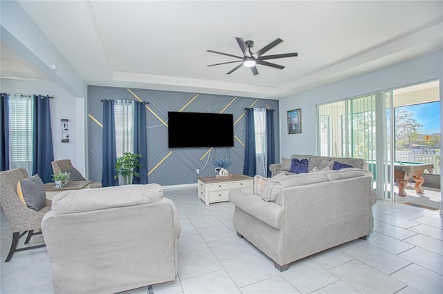 living room featuring an accent wall, a raised ceiling, ceiling fan, and light tile patterned floors