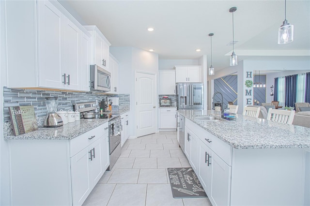 kitchen featuring white cabinets, decorative backsplash, a kitchen island with sink, stainless steel appliances, and light tile patterned flooring