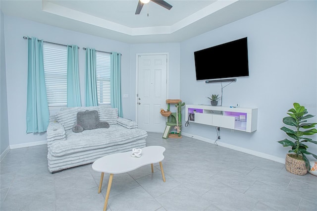 living area featuring a ceiling fan, a raised ceiling, and baseboards