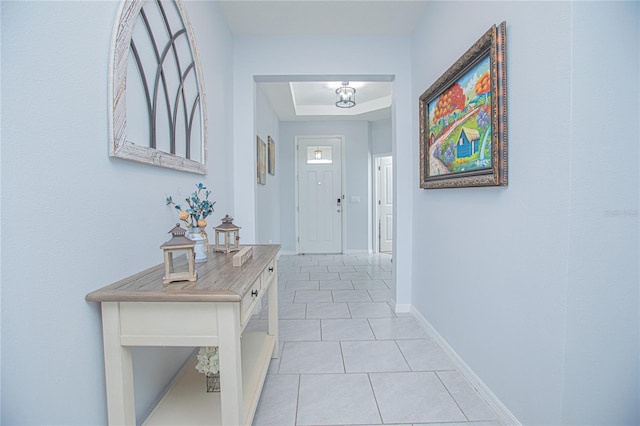 doorway featuring a tray ceiling, light tile patterned flooring, and baseboards